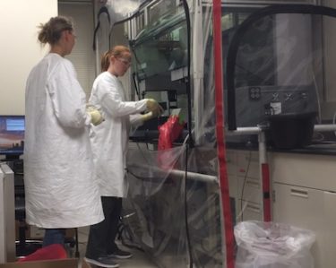 Cassie Simonich and Postdoc Lauren Noges use a large robotic machine to prepare blood samples.