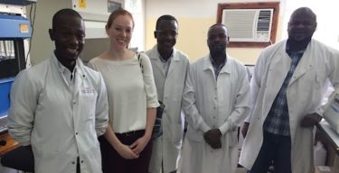 Four people wearing white lab coats stand with Cassie in a lab setting.