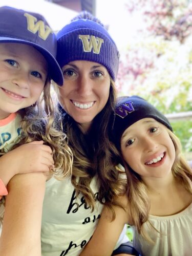 Perkins and her two daughters smile as they take a selfie. They all wear purple hats with a gold W.