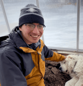 Justin Zeitlinger smiling at the camera while petting a white dog.